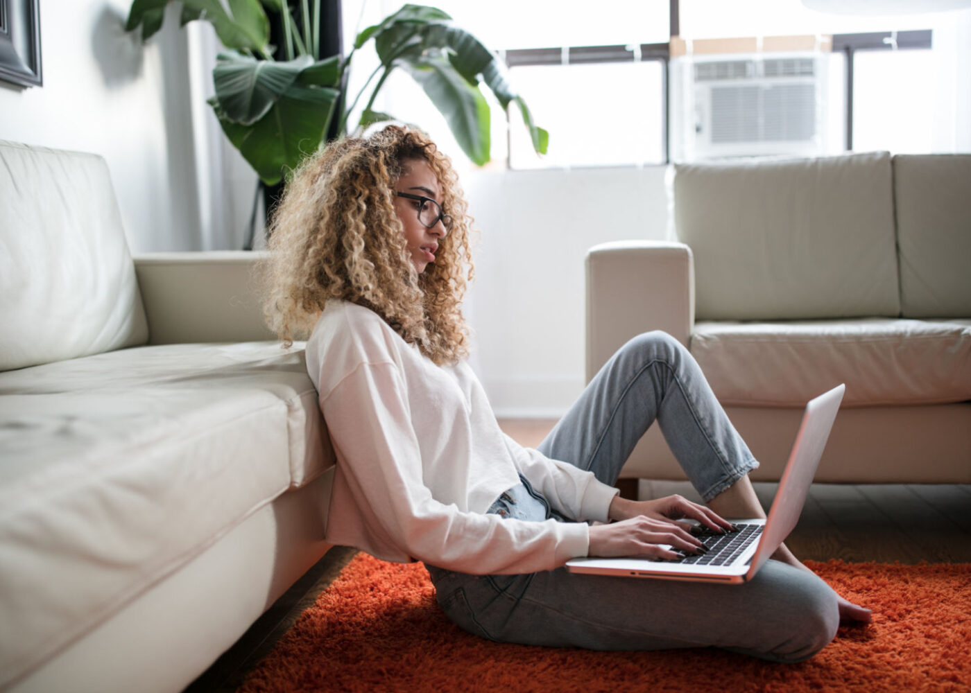 A woman sits on the floor, working her remote job in tech.