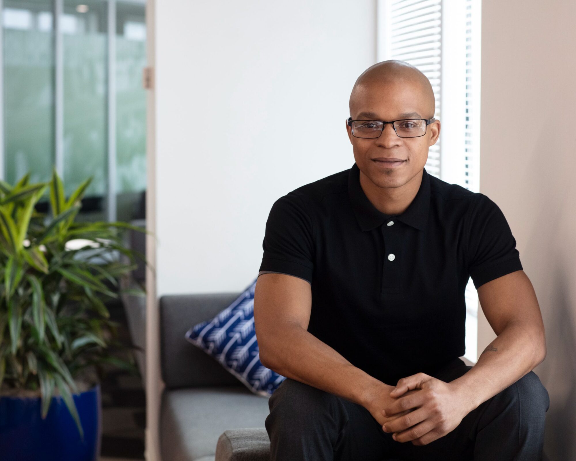 Image of a man wearing glasses smiling and sitting with arms folded.