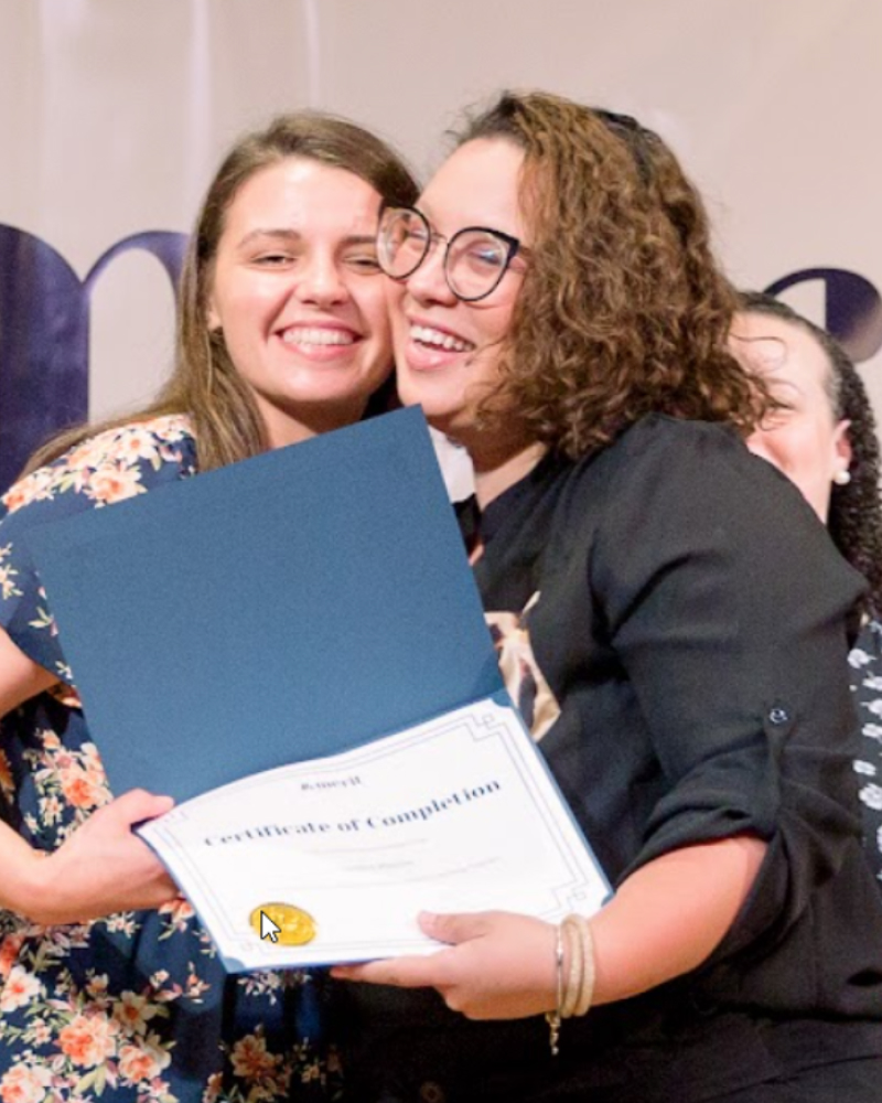 Two Merit America learners embracing, holding a Certificate of Completion