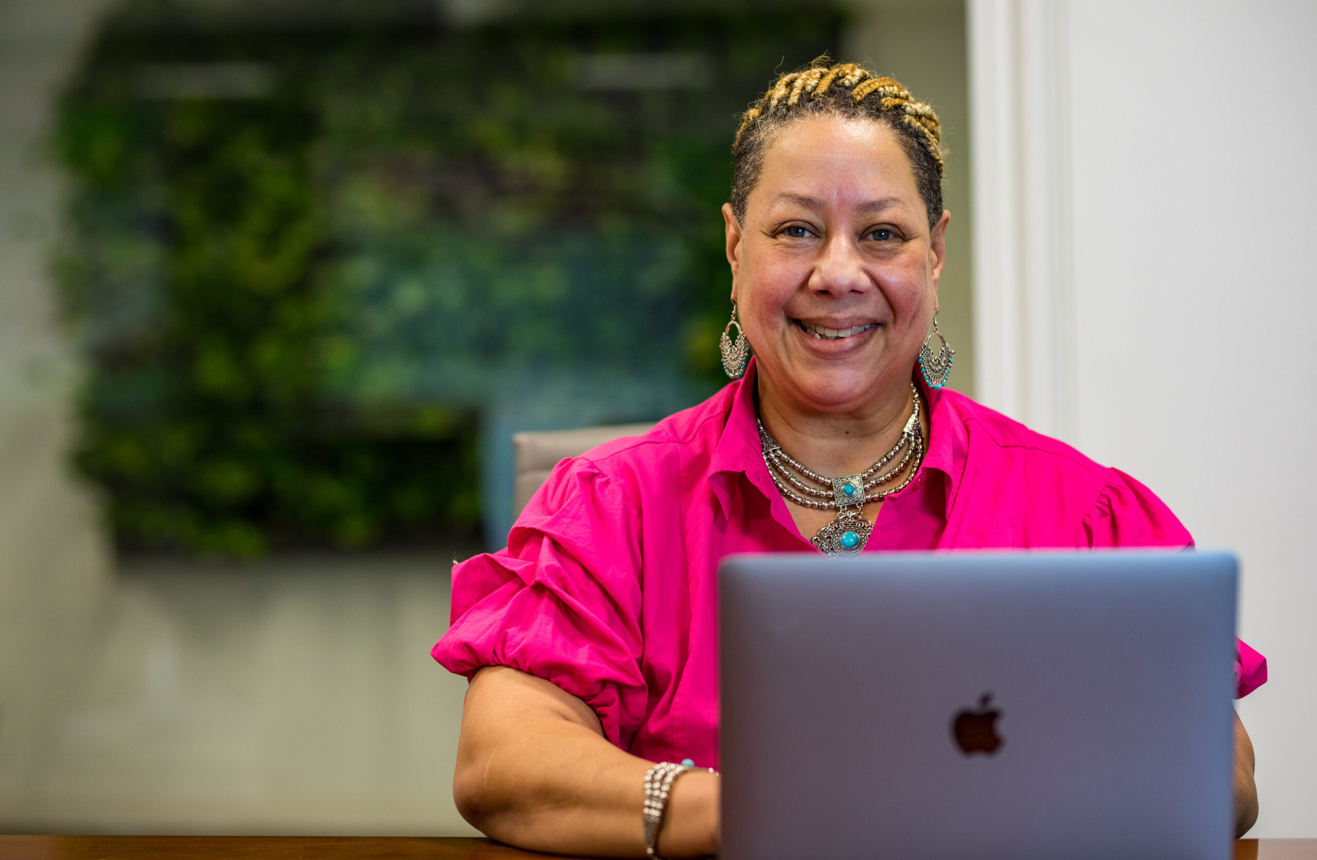 An alumn of the Merit America UX Design course smiles behind a laptop.