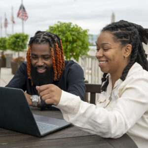 Two Merit America alumni pose while looking at a computer.