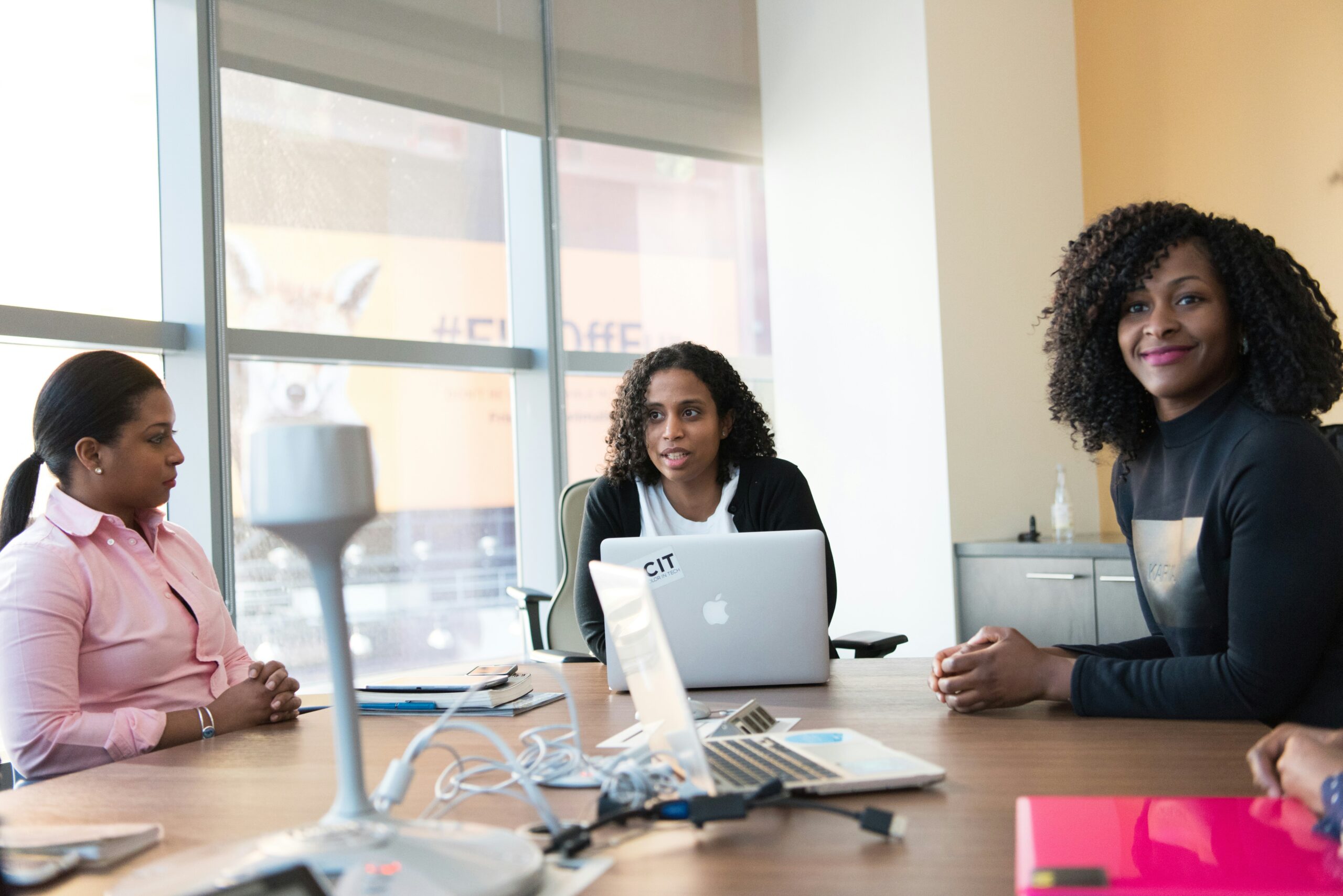 Three women in a conference room discussing solutions to their company's problems.