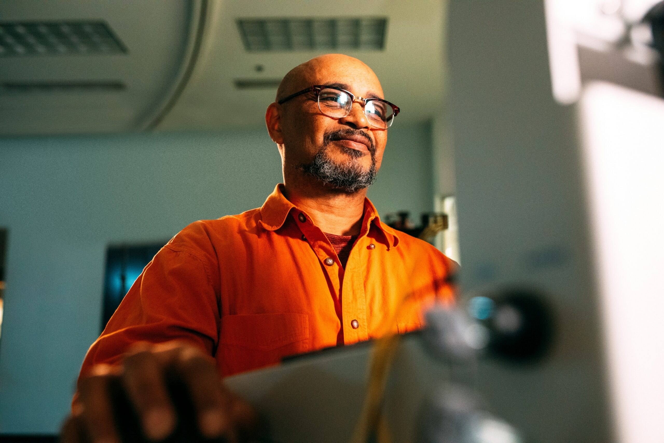 A man in an orange shirt looking up from a screen, mid-thought