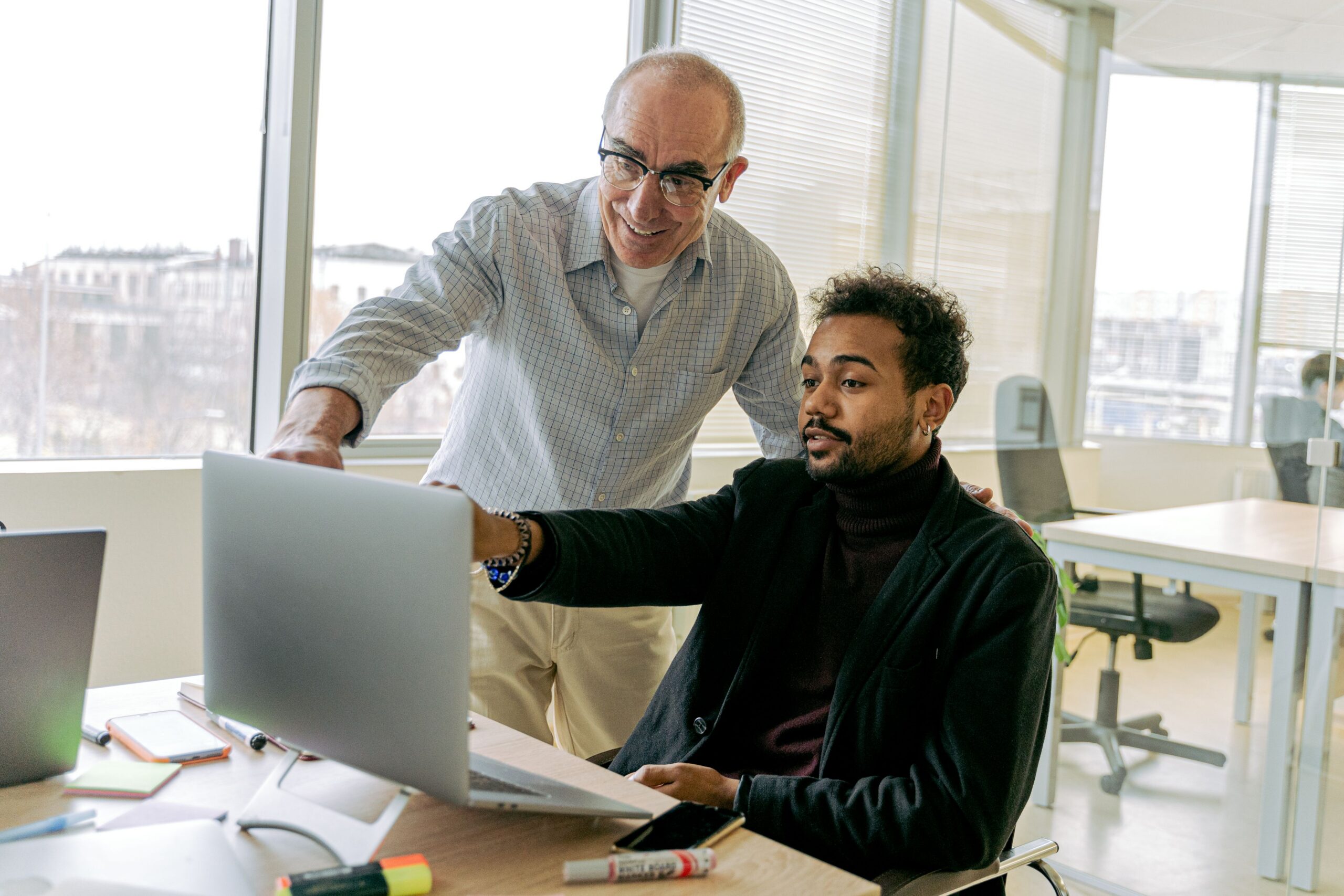 Two people at a desk, one helping the other through something on a laptop